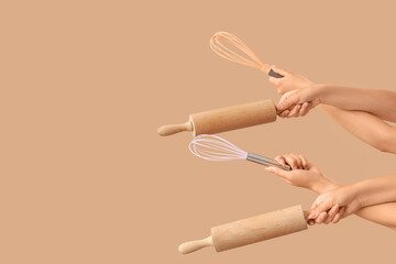 Female hands with rolling pins and whisks on beige background