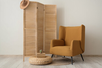 Comfortable armchair with folding screen and ottoman near white wall