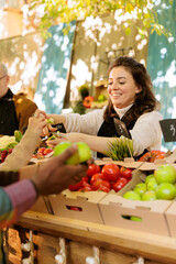 Diverse individuals receiving fruits samples at farmers market, browsing freshly harvested fruits and veggies at local farmers market. Smiling vendor giving apple slices to customers for tasting.