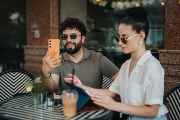 A man and woman having coffee together at an outdoor cafe, using a smart phone and studying a menu, showcasing friendship and collaboration.