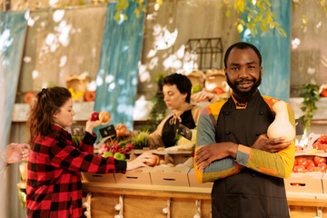 African american guy providing freshly harvested organic produce at greenmarket booth. Young small farm business owner standing near marketplace booth, grasping natural bio vegetable.