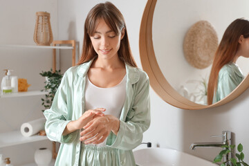 Morning of young woman applying cream onto her hand in bathroom