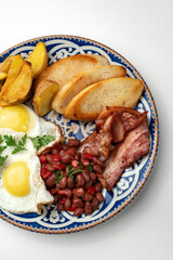 Delicious breakfast plate featuring eggs, beans, bacon, and potato wedges served on a decorative dish