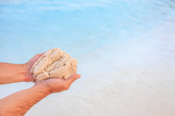 A person is holding a handful of sand on a beach