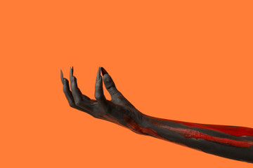 Black witch hand with claws on orange background. Halloween celebration
