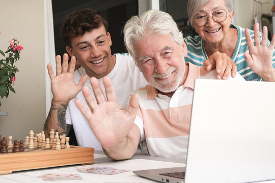 Video call. Happy multi generation family enjoying free time together sitting outdoors on terrace smiling waving hands to webcam laptop. Grandparents and young grandson using modern technology