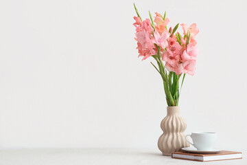 Vase with bouquet of beautiful gladiolus flowers, book and cup of coffee on table against white background