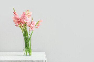 Glass vase with bouquet of beautiful gladiolus flowers on table against white background