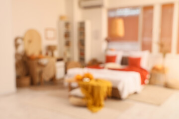 Interior of stylish bedroom with comfortable workplace, coffee table, plaid and pumpkins, blurred view