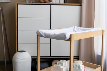 Empty nursery with changing table with diapers, lamp, commode and window with simple curtains