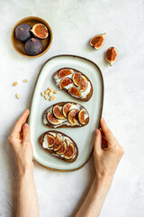 Hands are holding the plate of figs sandwiches with cheese and honey for breakfast. Top view