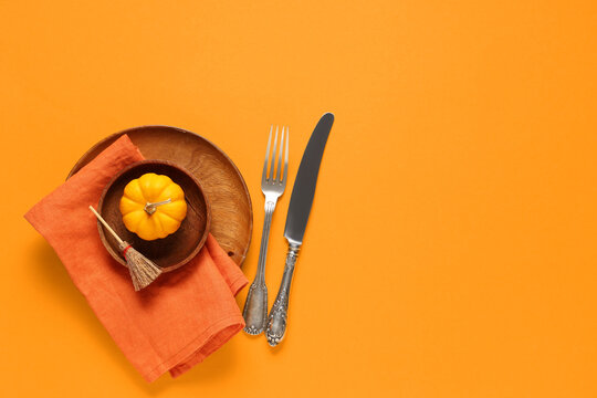 Beautiful table setting with fresh pumpkin and broom for Halloween celebration on orange background