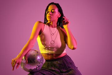 Beautiful young African-American woman with braids holding disco ball on color background