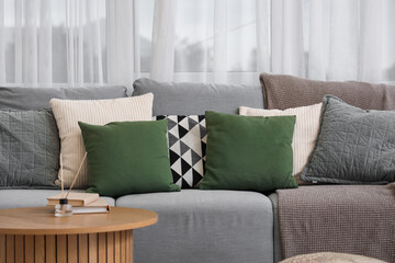 Soft cushions with plaid on grey sofa in living room