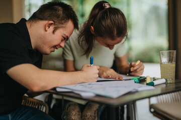 Naklejka premium A joyful moment with young friends, including a male with Down syndrome and a girl in a wheelchair, drawing and painting together at a table.
