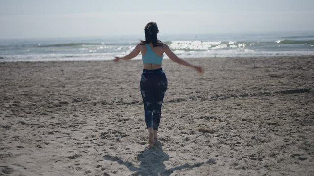 young girl long-haired brunette Caucasian woman walking backwards on the sand of the beach on a sunny day fans herself by moving her hands