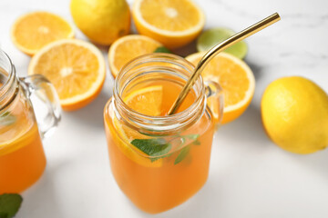 Mason jars of fresh orange juice with mint and different citrus fruits on white background