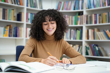 Cute young curly-haired woman sitting at the table in the library