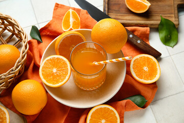 Glass of fresh orange juice and plate with fruits on white tile background