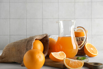Jug of fresh orange juice and sack bag with fruits on white table