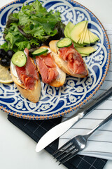 Colorful plate of smoked salmon sandwiches with cucumbers, greens, and olives on a decorative blue platter