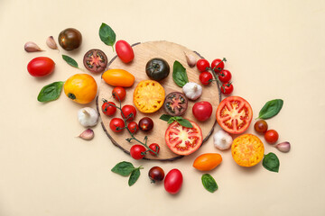 Wooden board with different fresh tomatoes, garlic and basil on beige background