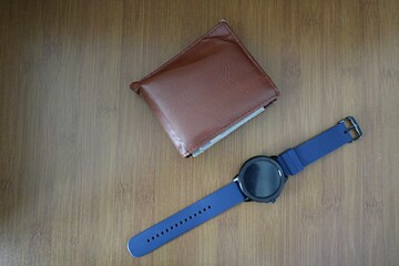 Brown wallet and watch are placed on the wooden table.