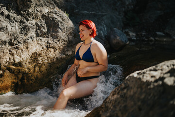 A joyful woman with red hair cooling off in the river at the mountain, enjoying refreshing water and a natural setting