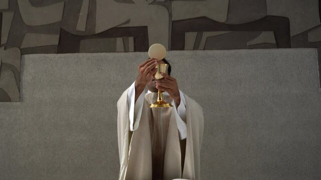 Priest raising the host and wine during the final doxology at a Catholic church mass.