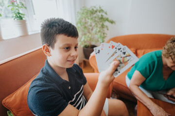 A cheerful young boy engages in a card game with a family member in a cozy living room setting, showing excitement and joy.