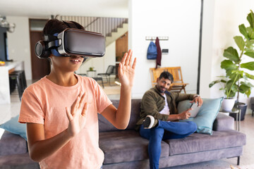 Using VR headset, Indian boy exploring virtual world while indian father watches on couch