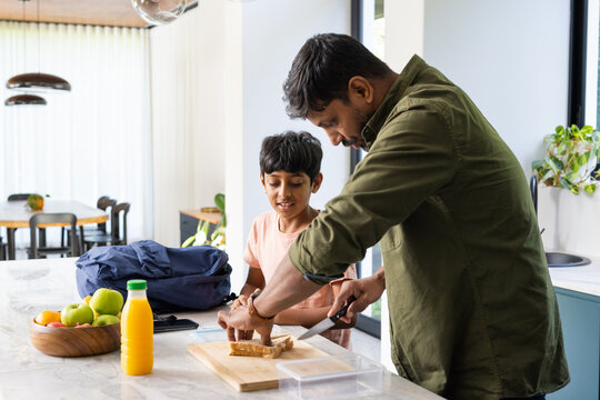 indian father preparing lunch with son in kitchen, cutting bread on cutting board