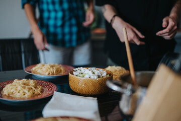 Two individuals stand near a table filled with plates of pasta and a bowl of fresh salad. The scene conveys a cozy and inviting atmosphere, perfect for home-cooked meals.