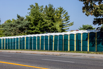 An extensive line of green and yellow outdoor portable toilets for a music event beside a road with...