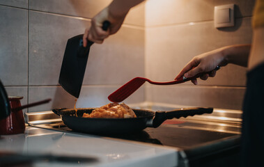 Close-up of hands cooking food in a frying pan on a kitchen stove, showcasing culinary skills and the joy of homemade meals.