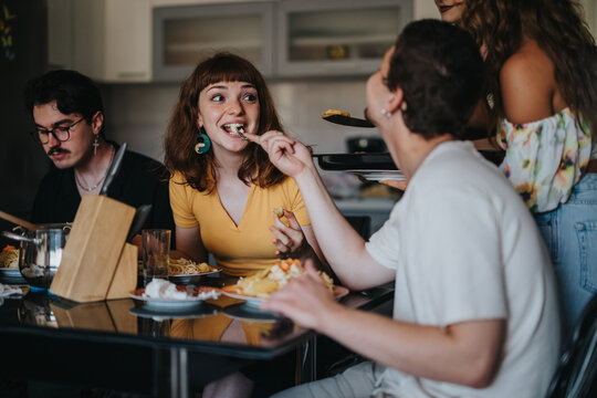 A cheerful group of young friends sit around a dining table, sharing a meal and engaging in lively conversation in a cozy home setting.