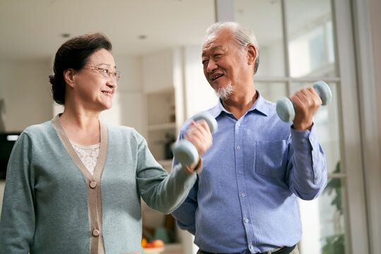 happy senior asian couple exercising at home using dumbbells