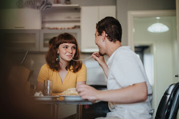 Fototapeta premium A happy couple sharing a playful moment while having dinner together in a cozy kitchen setting, symbolizing love and companionship.