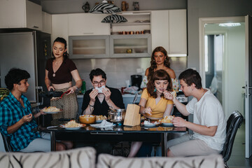 Obraz premium A group of young friends sharing a meal in a modern kitchen, creating a warm and friendly atmosphere. The scene captures togetherness and casual dining at home.