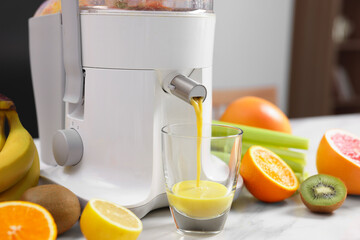 Modern juicer, fresh fruits and glass on white marble table in kitchen