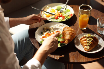 Man having tasty breakfast at wooden table in cafe, closeup
