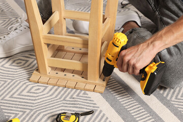 Man repairing wooden stool with electric screwdriver indoors, closeup