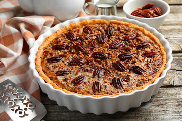 Delicious pecan pie in baking dish and cake server on wooden table, closeup