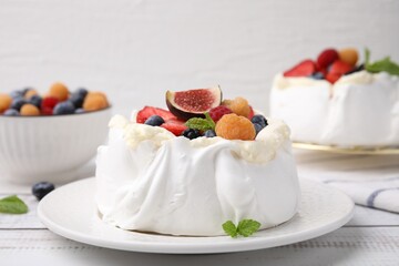 Pavlova cake (meringue dessert) with whipped cream, fresh berries, fig and mint on white wooden table, closeup