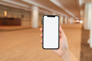Hand holding black smartphone with blank screen for graphic display montage at shopping mall background.