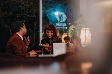 A joyful couple shares an evening at a stylish restaurant, enjoying drinks and heartfelt conversation. Warm lighting creates a cozy and romantic atmosphere.