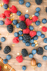 Close-up composition, assorted mix berries: blackberries, blueberries, raspberries top view flat lay in a plate. Isolated on a wooden table background, vertical image