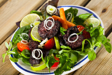 Tasty black pudding sausage served with vegetables, onion and greens on plate