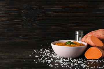 Mashed sweet potatoes in bowl, sweet potato and salt on wooden background, space for text