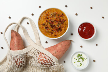 Mashed sweet potatoes in bowl, sauces and sweet potatoes in string bag on white background, top view